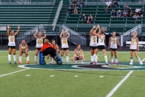 Girls' field hockey team celebrating on the field, showcasing team spirit and athleticism during a game.