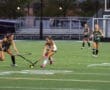 Field hockey players compete on a green turf field, showcasing teamwork and athleticism during a game.