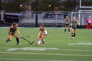 Field hockey players compete on a green turf field, showcasing teamwork and athleticism during a game.