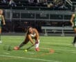 High school field hockey players compete under stadium lights; a player lunges to hit the ball on the field.