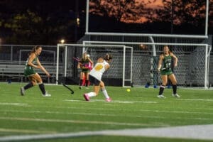 Field hockey players in action during an evening match on a stadium field, showcasing dynamic gameplay and teamwork.
