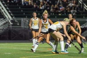 High school field hockey players in action during a nighttime game, showcasing teamwork and athletic skills.