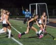 High school field hockey players compete under stadium lights, showcasing teamwork and athleticism on the turf.