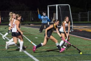 High school field hockey players compete under stadium lights, showcasing teamwork and athleticism on the turf.