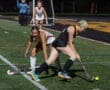 Field hockey players competing for the ball during a nighttime match on the turf field, showcasing athletic skill and teamwork.