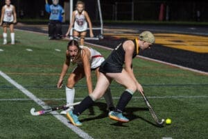 Field hockey players competing for the ball during a nighttime match on the turf field, showcasing athletic skill and teamwork.