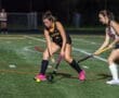 Field hockey match in action at night, featuring two players competing for the ball on a vibrant turf field.