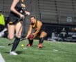 Field hockey players in action during a night game, focusing on a player making a critical move with the stick.