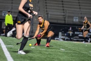 Field hockey players in action during a night game, focusing on a player making a critical move with the stick.