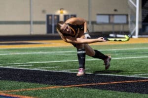 Field hockey player executes a powerful shot on goal under evening lights, showcasing skill and athleticism.