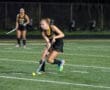 Field hockey player skillfully dribbling the ball on a turf field during a night game, focusing on team strategy.
