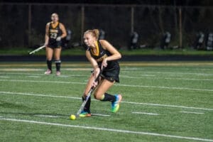 Field hockey player skillfully dribbling the ball on a turf field during a night game, focusing on team strategy.