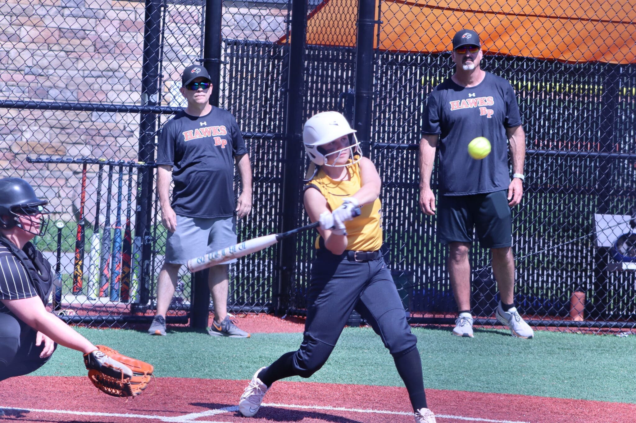 Young female softball player swings a bat while coaches observe during a practice at a sports facility.