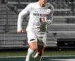 Player in white uniform of North Allegheny runs with the soccer ball during a night game on the field.