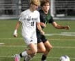 Two high school soccer players compete for the ball on a field at night, with action-packed intensity.