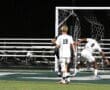 Soccer players in action as a shot on goal is taken during a night game, showcasing the intensity of the match.
