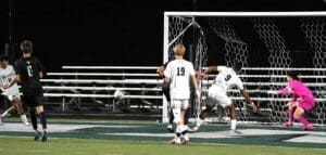 Soccer players in action as a shot on goal is taken during a night game, showcasing the intensity of the match.