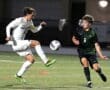 Two soccer players compete for the ball on a brightly lit field, showcasing skill and athleticism during a night game.