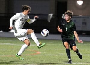 Two soccer players compete for the ball on a brightly lit field, showcasing skill and athleticism during a night game.