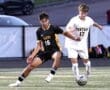 Two high school soccer players competing for the ball during a match, one in black and yellow, the other in white.