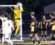 High school soccer goalie leaps to make a save during an exciting match, surrounded by teammates and opponents.