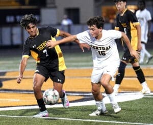 Two high school soccer players compete for the ball during a match, showcasing athleticism and teamwork on the field.