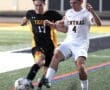 Two soccer players compete for the ball on the field, one in a black and yellow jersey, the other in white.