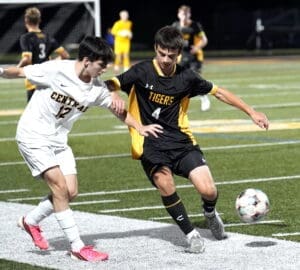 High school soccer match where players from Central and Tigers compete for the ball under stadium lights.