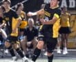 High school soccer player in action, running and kicking a ball during a competitive game at night.