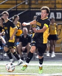 High school soccer player in action, running and kicking a ball during a competitive game at night.