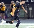 High school soccer player sprinting on the field while dribbling a ball during a nighttime game.