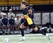 High school soccer player sprinting with the ball during a night game on the field, showcasing athletic skills.