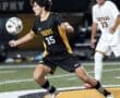 A soccer player in a black and yellow Tigers jersey controls the ball during an exciting match under stadium lights.