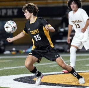 A soccer player in a black and yellow Tigers jersey controls the ball during an exciting match under stadium lights.