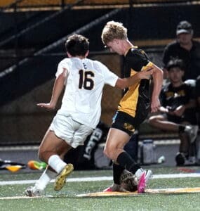 High school soccer players compete for possession of the ball during a nighttime match on a well-lit field.