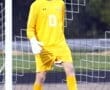 Young soccer goalkeeper in bright yellow kit, focused and ready on the field, with a soccer ball nearby.