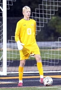 Young soccer goalkeeper in bright yellow kit, focused and ready on the field, with a soccer ball nearby.