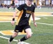 Young soccer player in a black and yellow Tigers uniform dribbling a ball on a green field during a game.