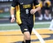 Young soccer player in black and yellow Tigers jersey dribbles a soccer ball on the field during a game.
