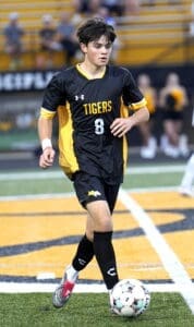 Young soccer player in black and yellow Tigers jersey dribbles a soccer ball on the field during a game.