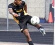 High school soccer player in black and yellow jersey executing a corner kick during an evening match.