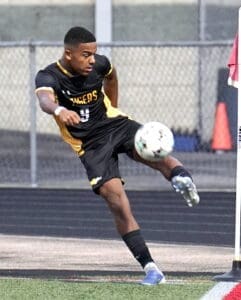 High school soccer player in black and yellow jersey executing a corner kick during an evening match.