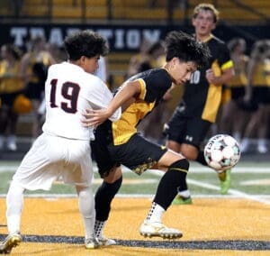 High school soccer players compete for the ball under stadium lights, showcasing dynamic athleticism and teamwork.