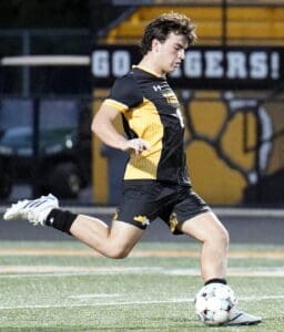 High school soccer player in action, kicking a soccer ball on the field during a game. Energetic and focused moment.