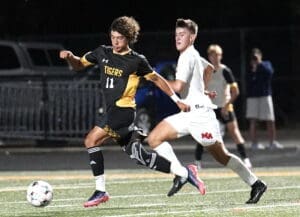 High school soccer players sprint for the ball in a dynamic game under stadium lights.