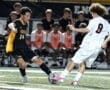High school soccer match featuring players in action, one in black jersey and the other in white, with spectators in the background.