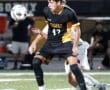 High school soccer player in black uniform preparing to intercept the ball during an intense game at night.