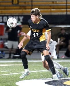 High school soccer player in black uniform preparing to intercept the ball during an intense game at night.