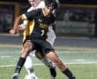Soccer players compete intensely for possession of the ball under stadium lights during a night game.