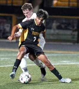 Soccer players compete intensely for possession of the ball under stadium lights during a night game.